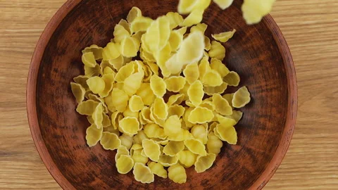 Shell-shaped pasta is poured into a brown ceramic bowl. 動画素材 304386654