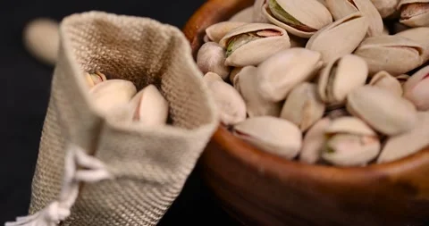 Shelled pistachio nuts with added salt in a wooden bowl and a linen bag, Stock Footage 310083253