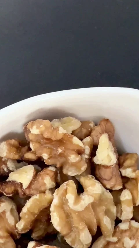 Shelled walnut halves are displayed in a white bowl Stock Footage 331980131