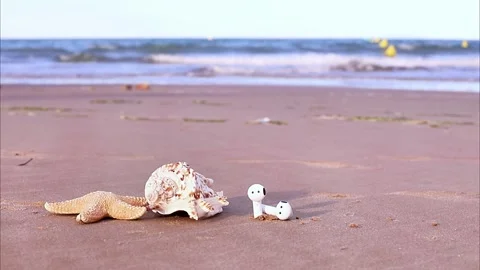 Shells and earbuds on a sandy beach near the ocean in bright daylight as wa.. Stock Footage 328760551