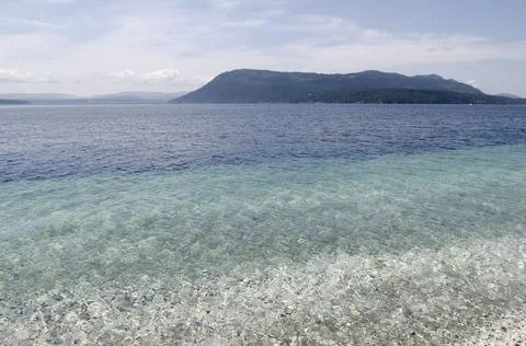 Shells and rocks beneath the clear water with Salt Spring Island in the backg Stock Photos