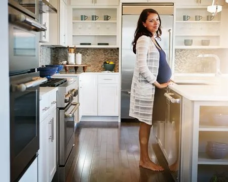 Shes got a bundle of joy on the way. a pregnant woman standing in her kitchen at Stock Photos