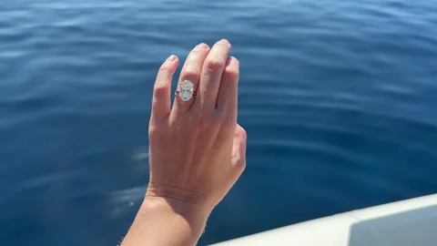 Shimmering diamond ring hand held against sparkling Mediterranean sea Stock Footage 319406896