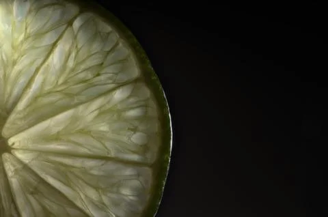 Shimmering lime segment radiates freshness against shadowy background Stock Photos