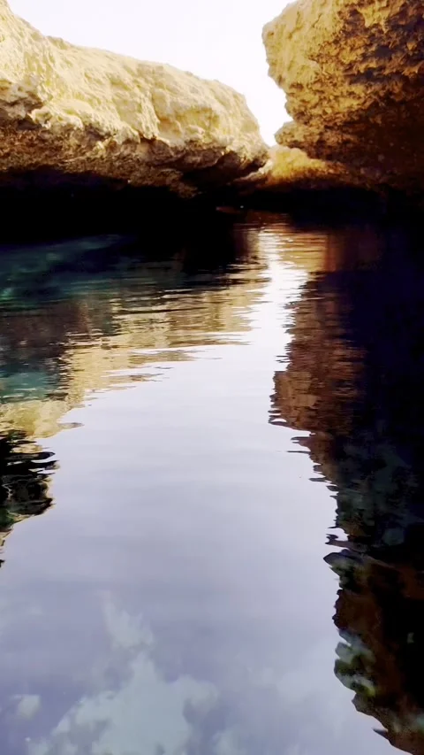 Shimmering reflections in turquoise lagoon inside rocky sea cave at sunset. G Stock Footage 329416411