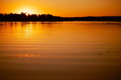 Shining lake with sun setting below horizon and covering with rays water surface Stock Photos