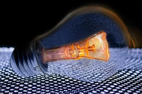 Shining light bulb on shining background mesh in front of black background. Stock Photos
