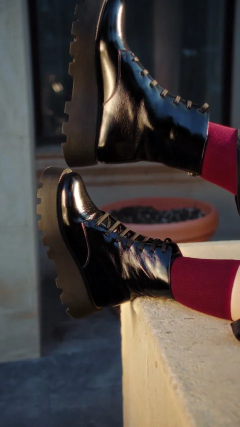 Shiny black combat boots on ledge with red tights Stock Footage 317335462