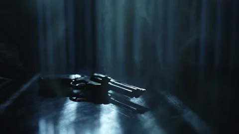 Shiny black revolver on a black table surrounded by smoke and backlight by 库存影片 290823966