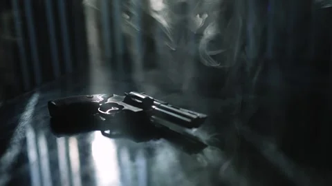 Shiny black revolver on a black table surrounded by smoke and backlight by Stock Footage 291919099