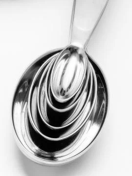 Shiny chrome kitchen measuring spoons nested together on white background. Stock Photos