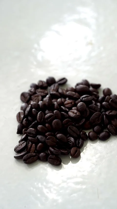Of shiny dark roasted coffee beans scattered on a white surface Stock Footage 344704829