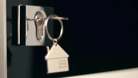 A shiny key with a chrome house keychain is inserted into a door lock Stock Footage 297775171