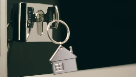 A shiny key with a chrome house keychain is inserted into a door lock Stock Footage 303300522