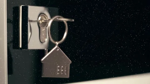 A shiny key with a chrome house keychain is inserted into a door lock Stock Footage 330894779