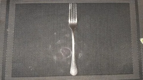 Shiny metal dinner fork placed on a dark textured mat 스톡 사진