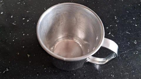 Shiny metal mug sits empty on a dark textured surface background 스톡 사진