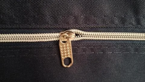 Shiny metal zipper pull attached to dark navy blue fabric material Stock Photos