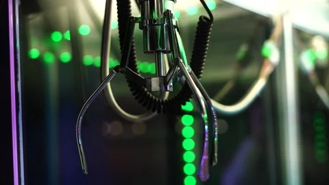 Shiny metallic claw machine grabber surrounded by colorful blurred arcade lights Stock Footage 323010219
