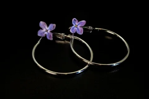Shiny round thin metal earrings and lilac flowers. Stock Photos