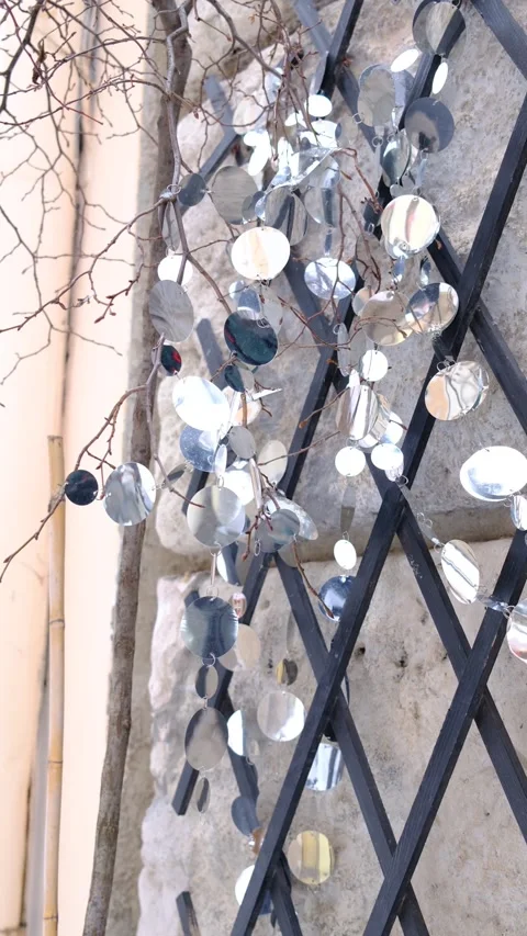 Shiny silver discs hang on bare tree branches next to a dark garden trellis Stock Footage 329242201