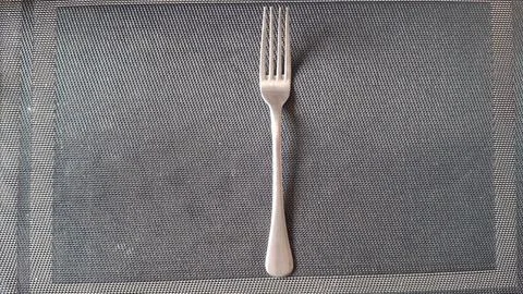 Shiny silver metal dinner fork centered on a dark textured mat 스톡 사진