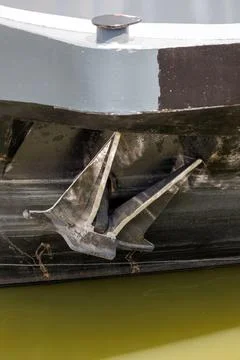 Ship anchor mounted on vessel bow above calm water in close up maritime detail Stock Photos