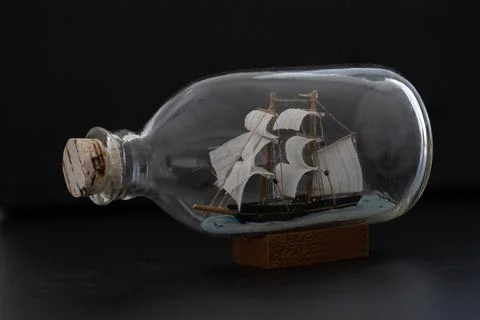 Ship in a Bottle. Small ship model in a bottle with a cork stopper on black b Stock Photos