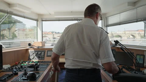 Ship captain stands at helm inside wheelhouse navigating toward Charles Bridge 動画素材 342321095