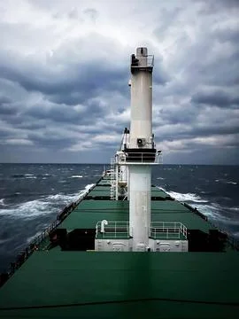 A ship cuts through the waves on the open sea against a cloudy sky 스톡 사진