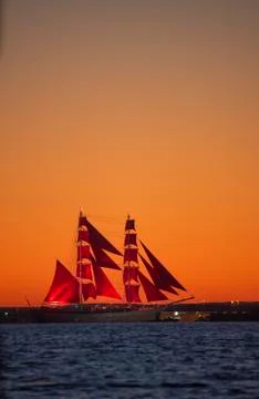 A ship with red sails at sunset on the background of a beautiful orange sky. Stock Photos