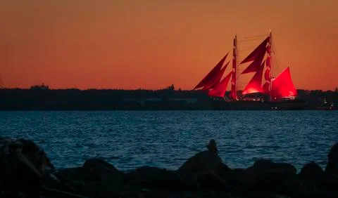 A ship with red sails at sunset on the background of a beautiful orange sky. Stock Photos