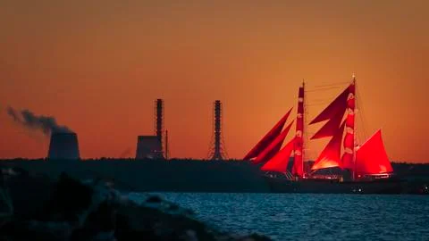 A ship with red sails at sunset on the background of a beautiful orange sky. Stock Photos