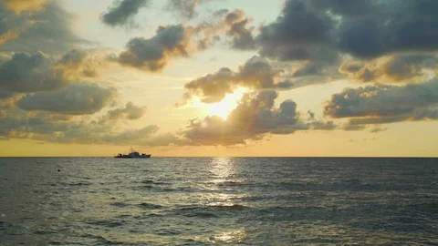 A ship sailing at sunset with backlit clouds in the sky Stock Footage 116046634