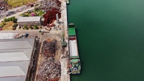Ship unloading materials at a dock near industrial area amid scrap piles 스톡 동영상 338324647