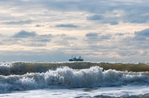 A ship on a wave against the background of clouds. Stock Photos