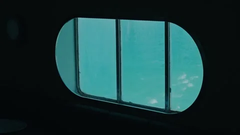 Ship Window Looking Out to Turquoise Sea From a Dark Cabin Interior Stock Footage 340595914