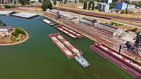 Shipping barges dock at a river port with buildings and train tracks nearby Stock Footage 344089129