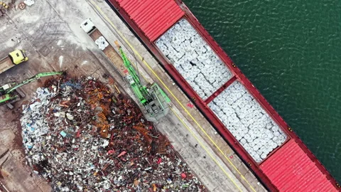 Shipping containers are loaded onto a cargo ship at a busy port while scrap Stock Footage 340929887