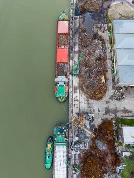 Ships unload materials at a port while cranes and storage areas are present.. Stock Photos