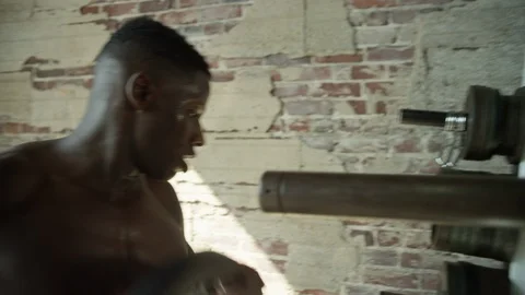 Shirtless African American changes weights on squat rack in industrial-style gym 動画素材 124462593