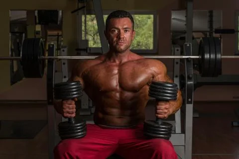 Shirtless body builder posing with dumbbell at the bench Stock Photos