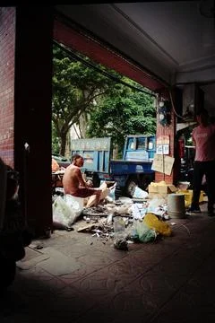 Shirtless elderly man sorting through garbage under Taipei arcade poverty Stock-Fotos