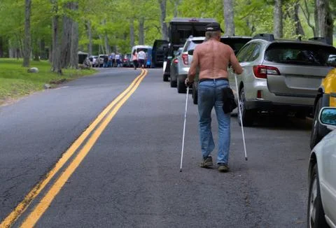 Shirtless elderly man walking with skiing poles on a road packed with parked  Stock Photos