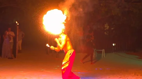 Shirtless fire-eater performing during carnival at beach, spectators watching Stock Footage 128853550