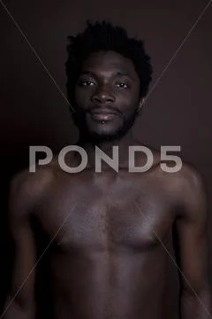 A shirtless hip young man standing against a brown background, waist up Stock Photos