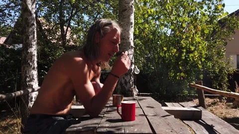 Shirtless long haired man smoking cigarette and drinking coffee Stock Footage 345485780