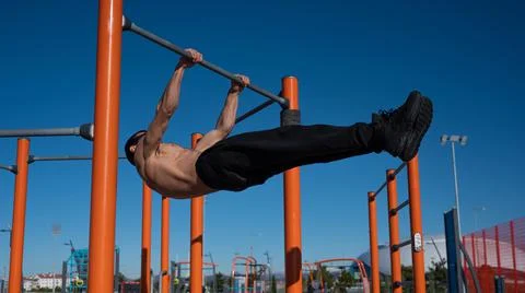 Shirtless man doing blanche on horizontal bar outdoors. Stock-Fotos