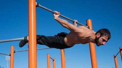 Shirtless man doing blanche on horizontal bar outdoors. Stock-Fotos