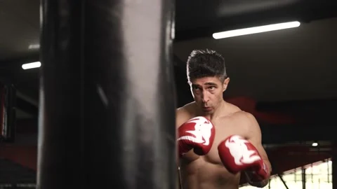 Shirtless man doing boxing in gym, feverishly hitting the sandbag heavily Stock Footage 201403596